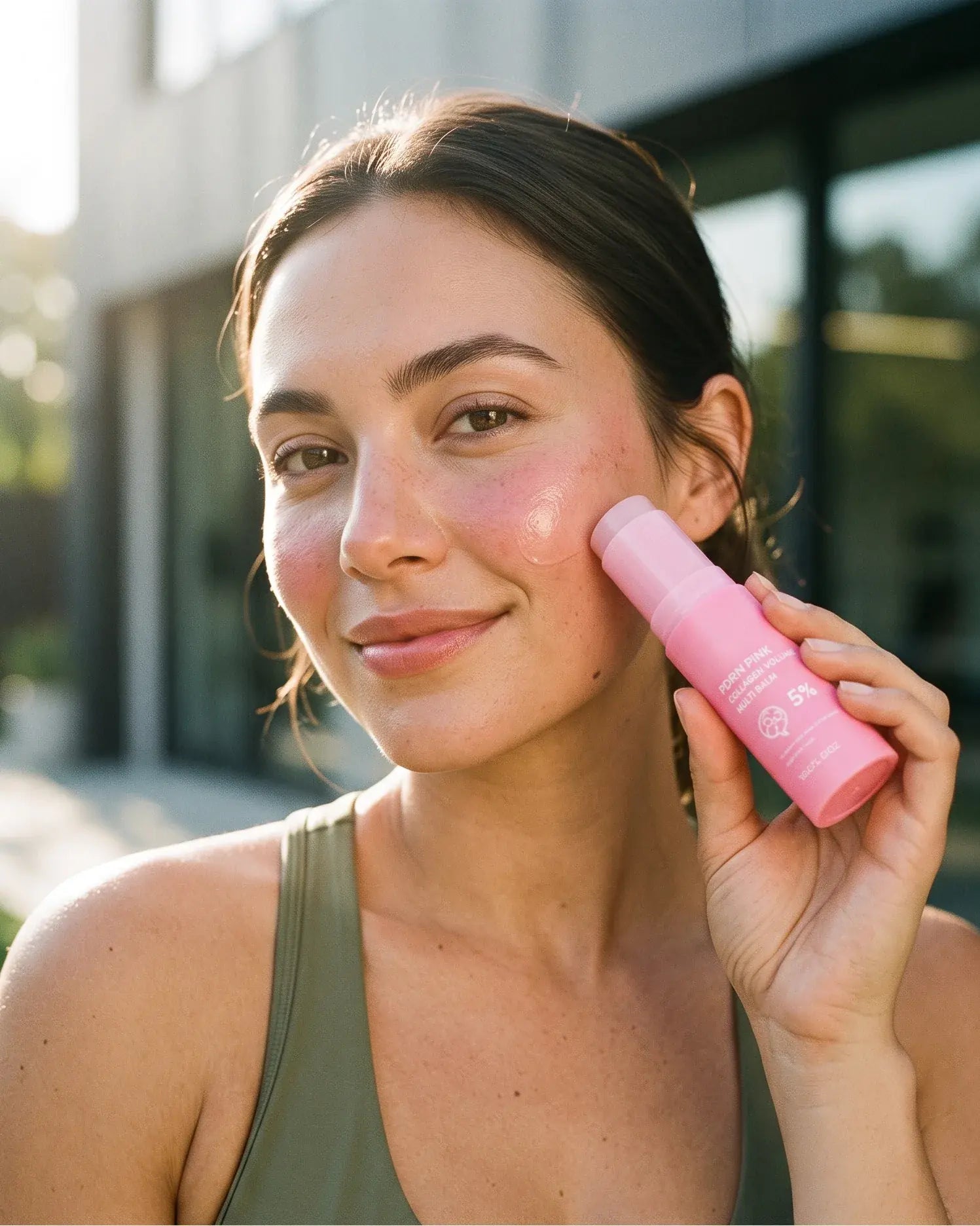 Woman holding the Volée Pink Balm beside her face, fresh dewy skin